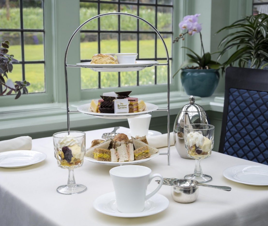 An assortment of bite size sandwiches and desserts served on a three tiered stand set on a table for two with white linens.