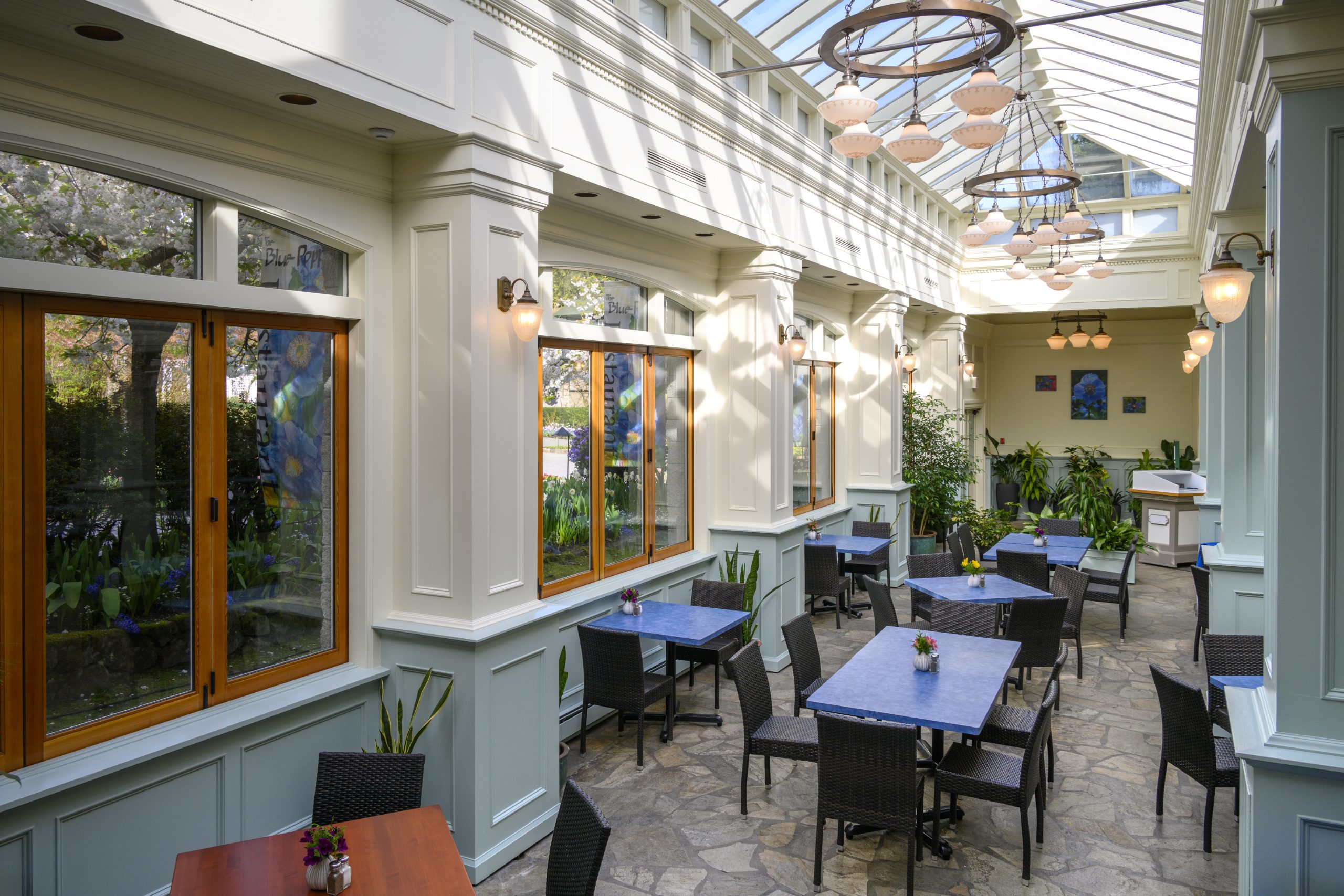 Tables and chairs set with floral arrangements inside the Blue Poppy Restaurant. Large windows and skylights offer a bright setting to dine in.