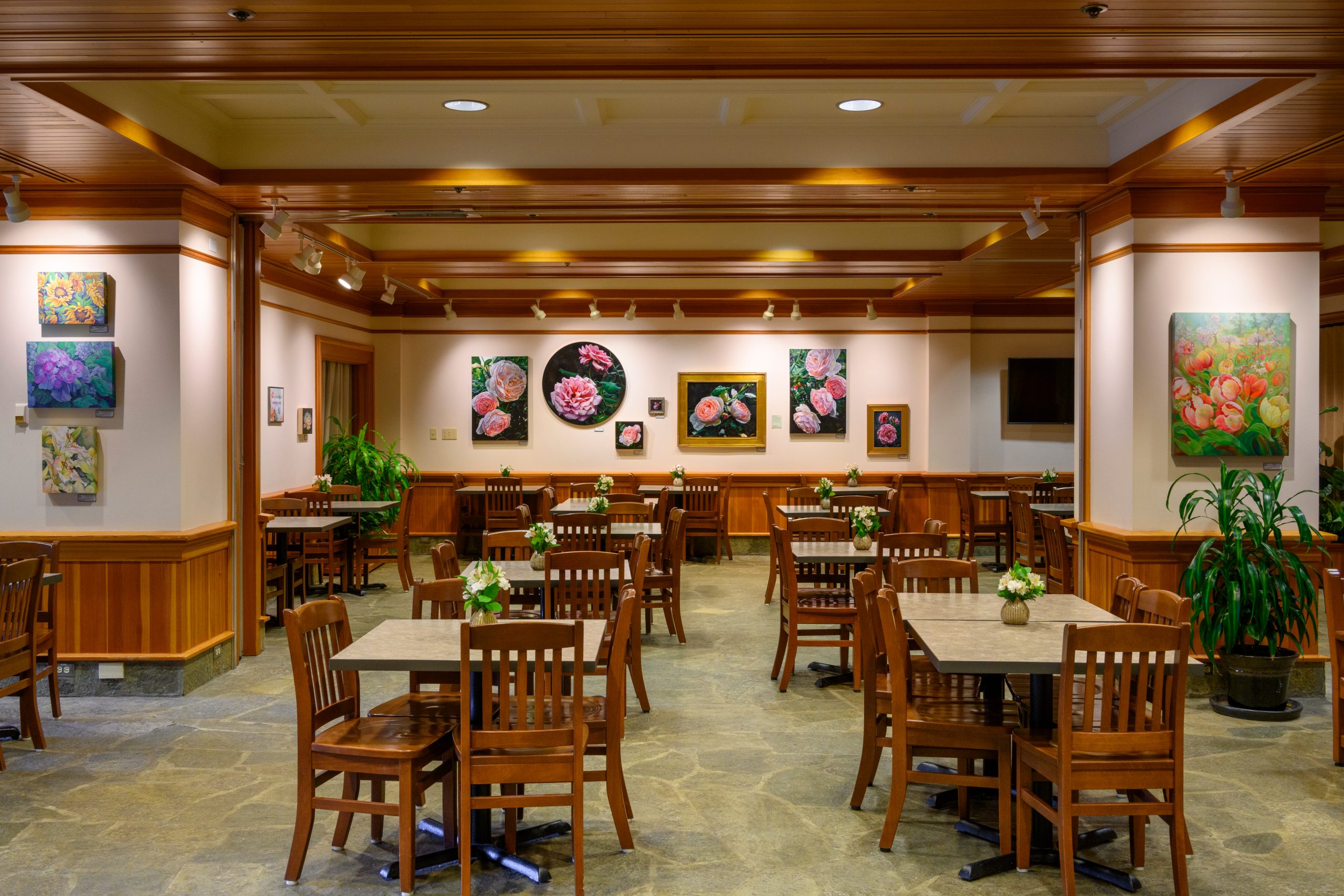 Tables and chairs set with flower arrangements inside the Coffee Shop. Artwork from local artists is featured on the walls.