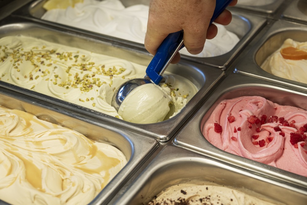Hand scooping gelato from it's metal serving container. Several more flavours are visible.