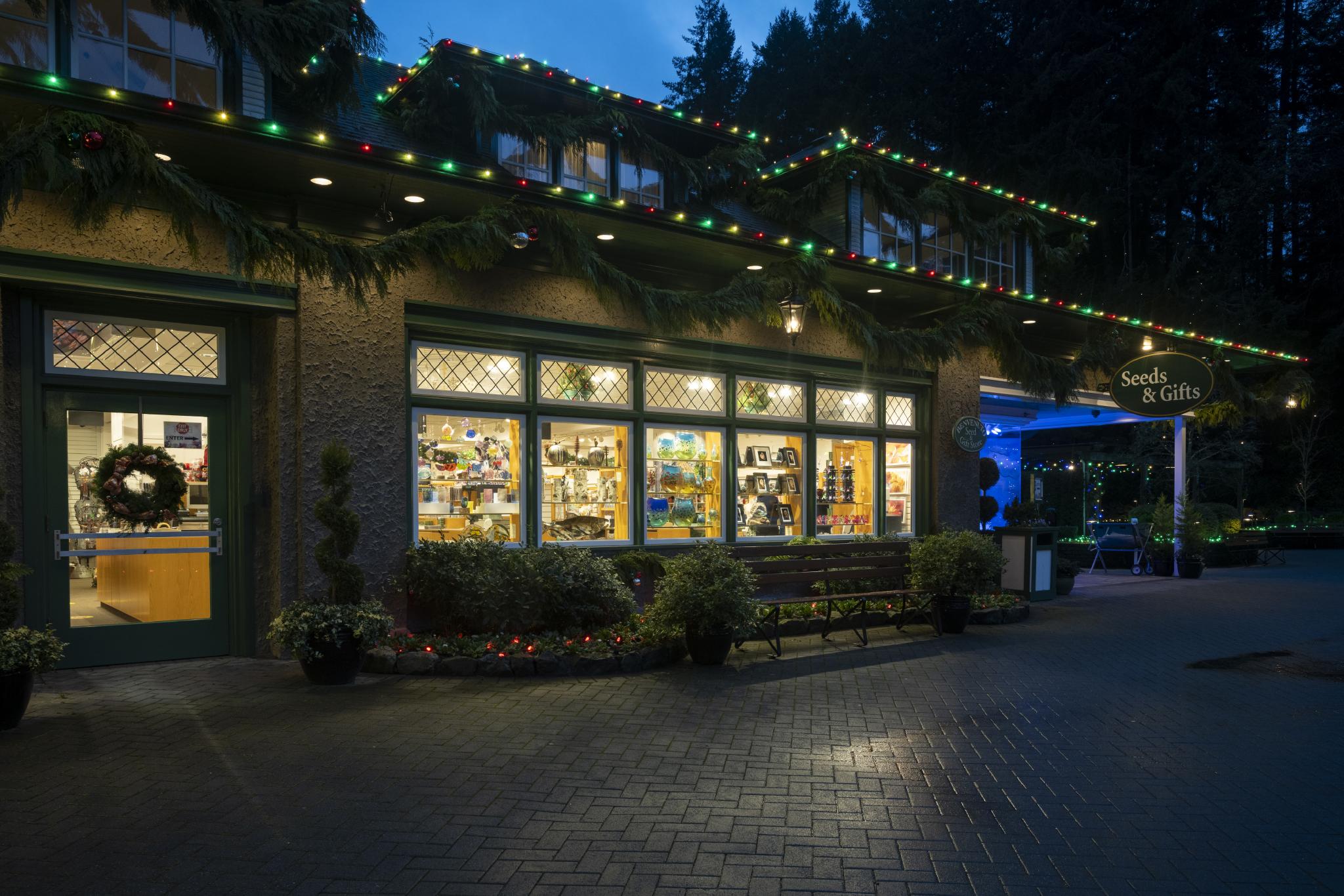 Vue extérieure du magasin Seed & Gift Store pendant la période de Noël. Des lumières de Noël rouges, vertes et blanches tapissent le toit du magasin Seed & Gift Store, tandis que des arcs en cèdre pendent sur les côtés du toit.